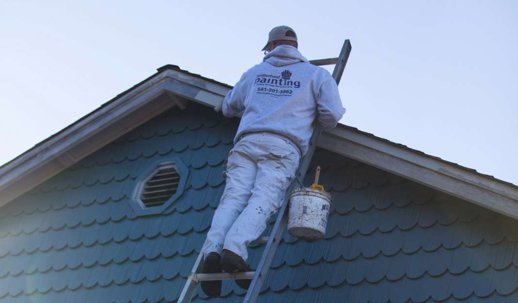 man on ladder painting a roof